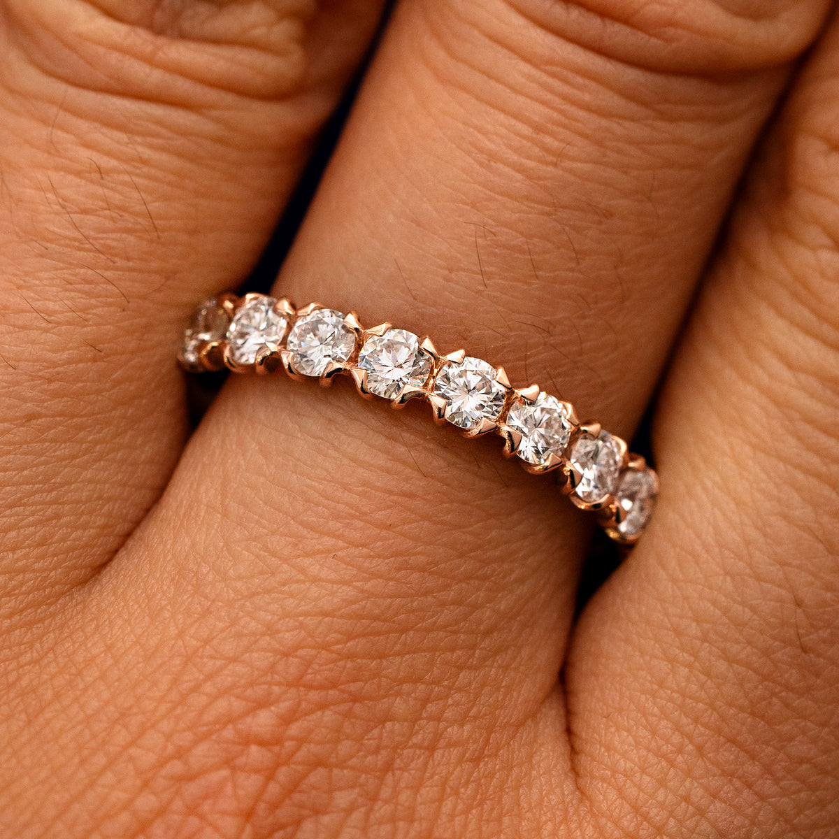 Close up view of a model's fingers wearing a 14k rose gold Petal Set Diamond Eternity Band