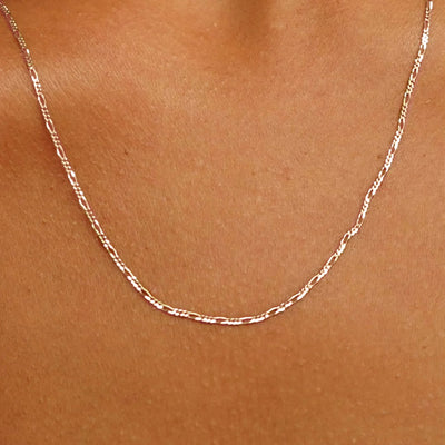 Close up view of a model's neck wearing a rose yellow gold Figaro Chain