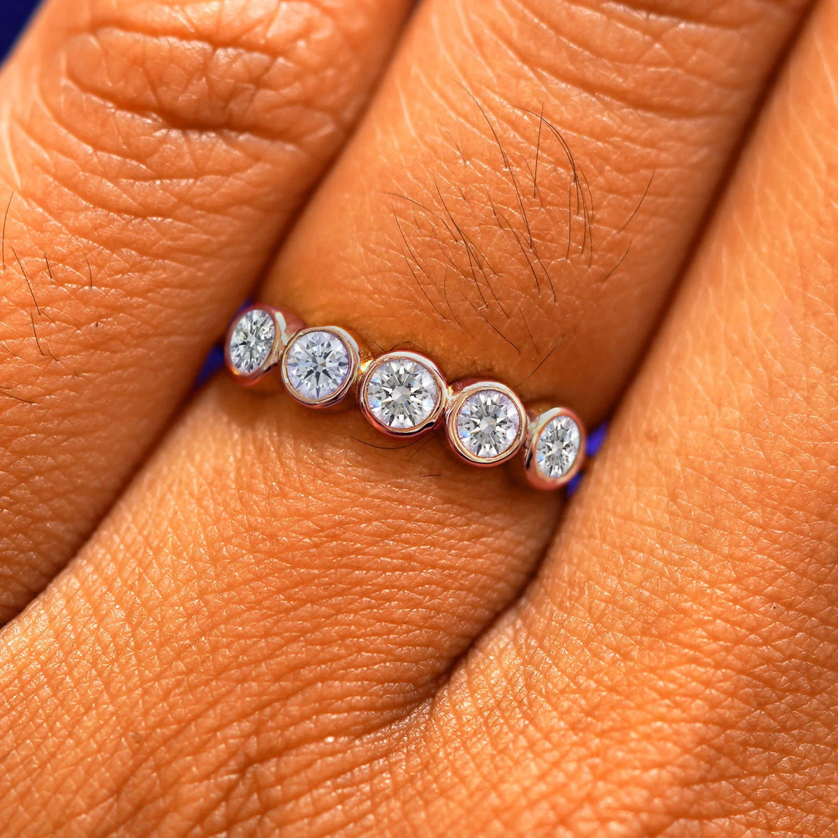 Close up view of a model's fingers wearing a 14k rose gold Five Diamond Ring with clear diamonds