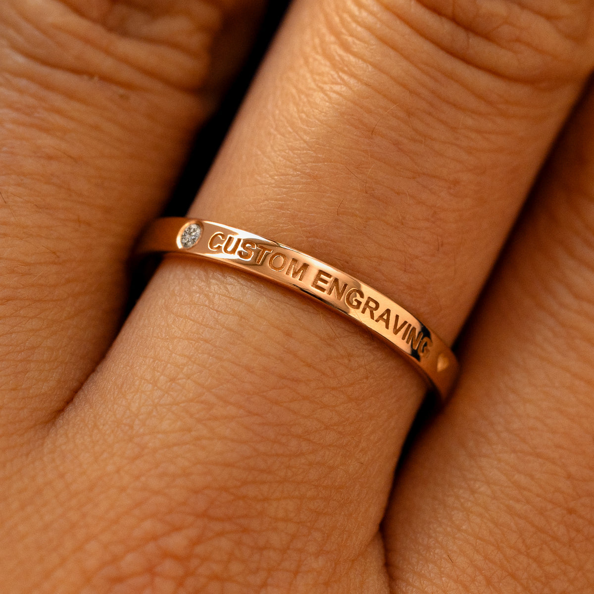 A model's finger wearing a diamond rose gold flush gemstone industrial band the words custom engraving on the top