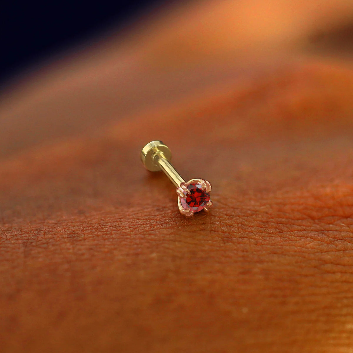 A solid 14k rose gold Garnet Flatback Piercing resting on the back of a model's hand