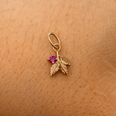 A solid 14k rose gold ruby Gemstone 3 Leaves Charm resting on the back of a model's hand
