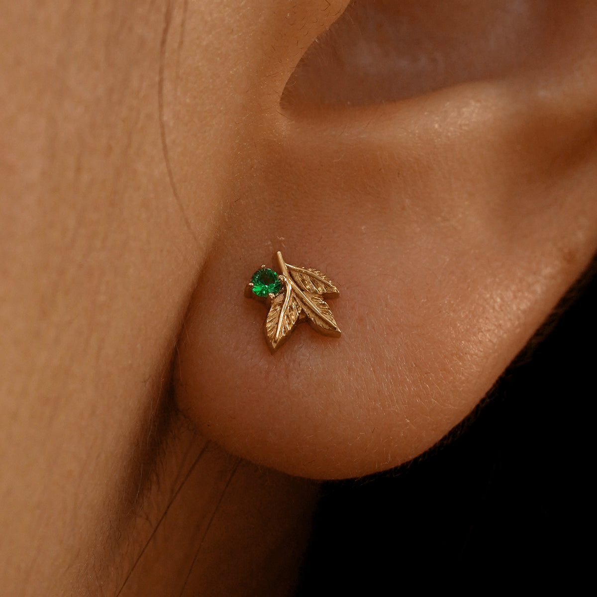 Close up view of a model's ear wearing a 14k rose gold emerald 3 Leaves Gemstone Earring