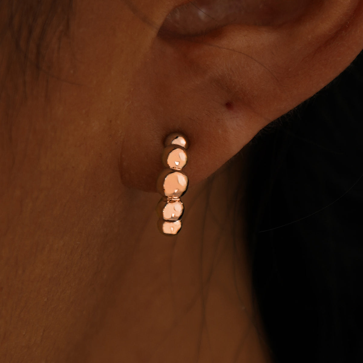 Close up view of a model's ear wearing a 14k rose gold Graduated Puffy Beaded Hoop