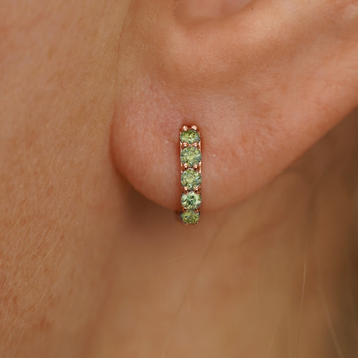 Close up view of a model's ear wearing a rose gold Mini Light Green Lab Diamond Huggie Hoop