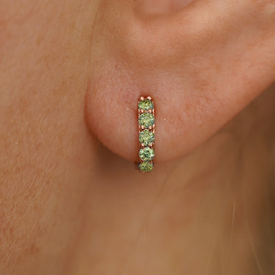 Close up view of a model's ear wearing a rose gold Mini Light Green Lab Diamond Huggie Hoop