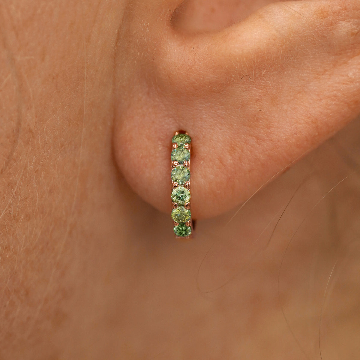 Close up view of a model's ear wearing a rose gold Small Light Green Lab Diamond Huggie Hoop