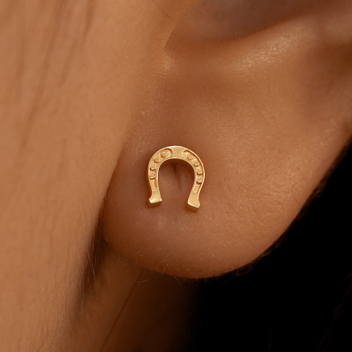 Close up view of a model's ear wearing a 14k rose gold Horseshoe Earring