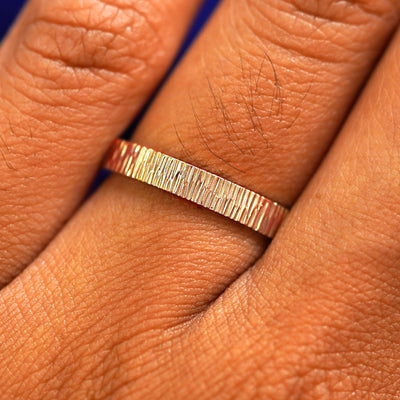 Close up view of a model's fingers wearing a 14k rose gold Industrial Wood Band