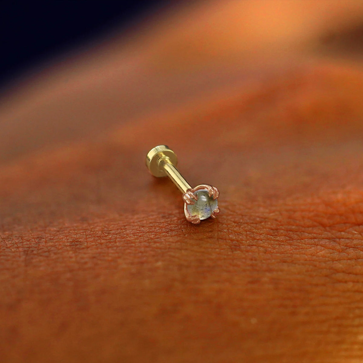 A solid 14k rose gold labradorite Flatback Piercing resting on the back of a model's 