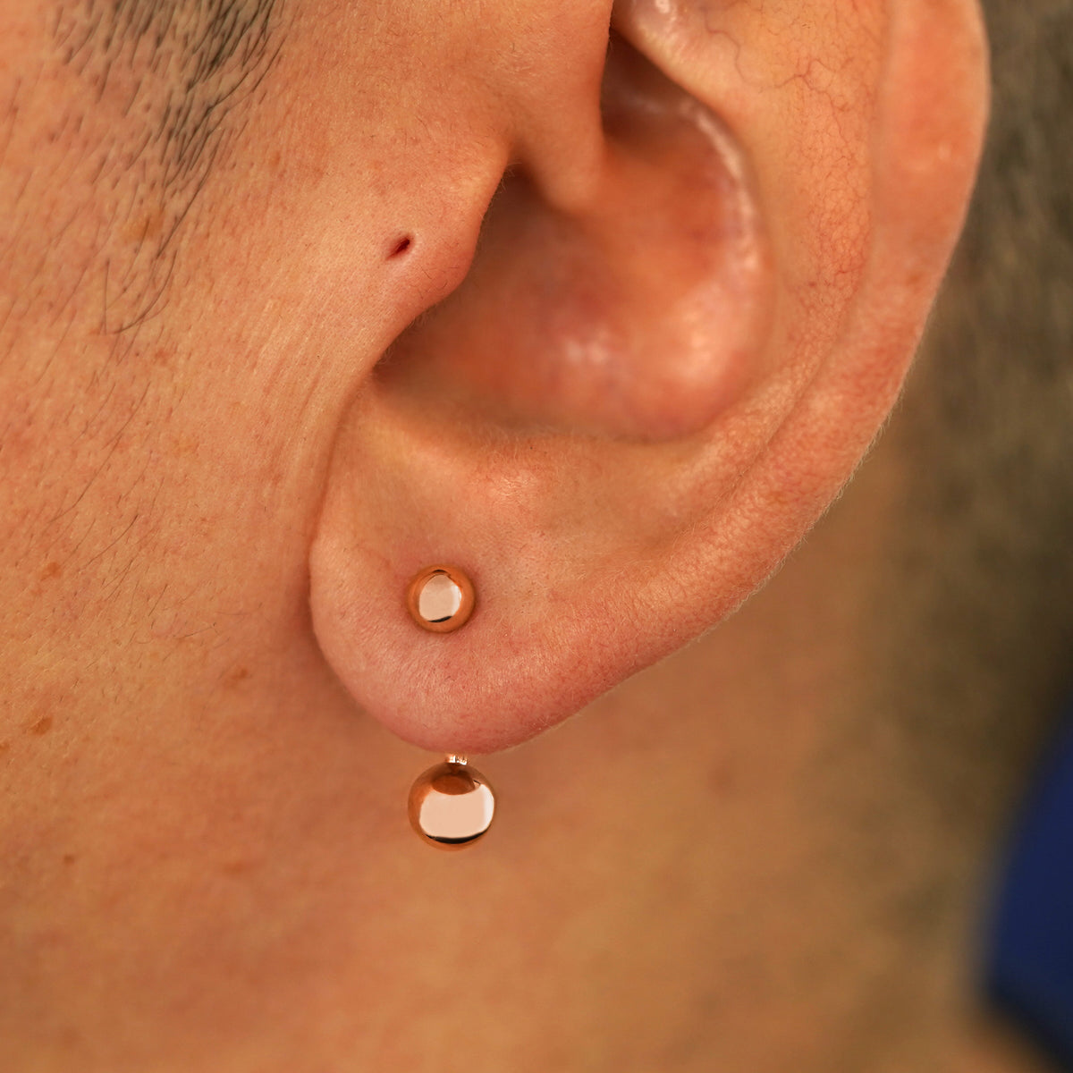 Close up view of a model's ear wearing a 14k rose gold Large Curved Barbell through a lobe piercing