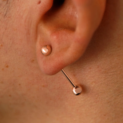 Close up view of a model's ear wearing a 14k rose gold Large Straight Barbell through a lobe piercing