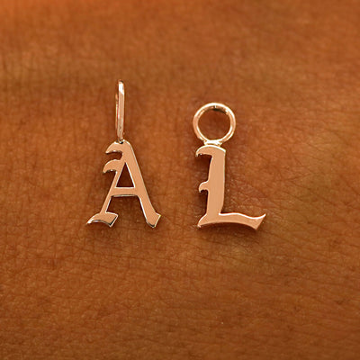 A solid 14k rose gold Initial Charm for earring in the letter A and L laying on the back of a model's hand