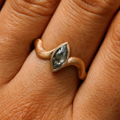 Close up view of a model's hand wearing a 14k rose gold marquise cabochon salt and pepper diamond engagement ring