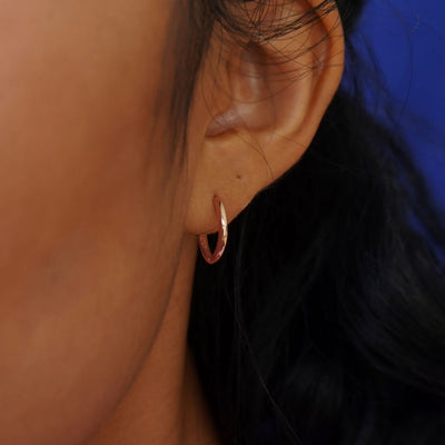 A model's ear wearing a 14k rose solid gold Medium Curvy Huggie Hoop