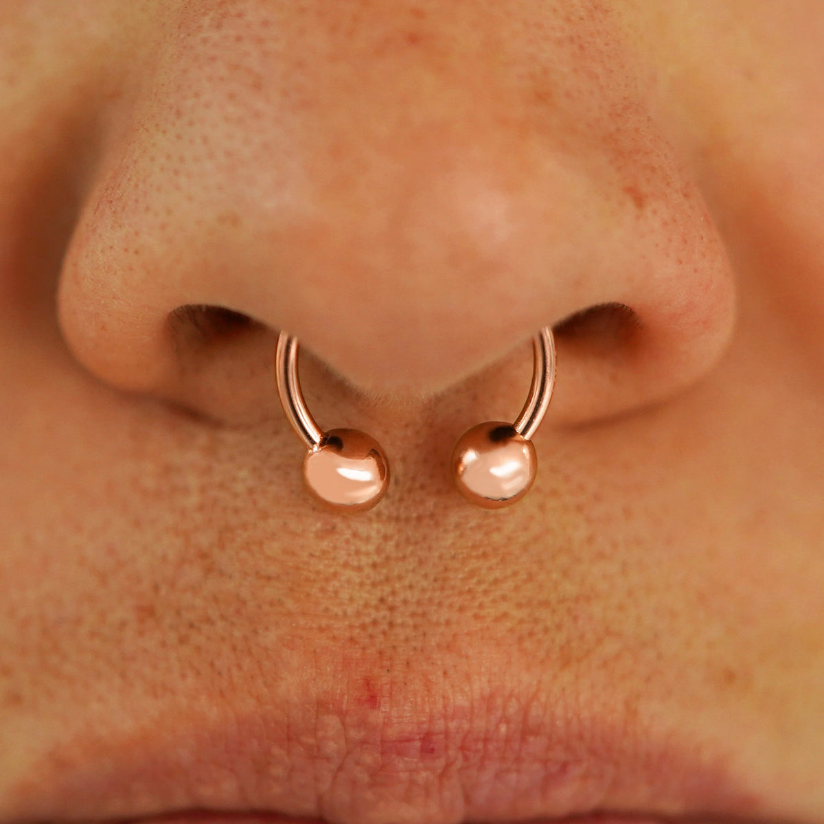 Close up view of a model's nose wearing a 14k rose gold Medium Horseshoe in a septum piercing