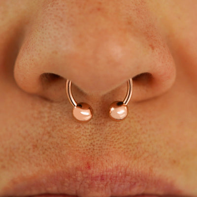 Close up view of a model's nose wearing a 14k rose gold Medium Horseshoe in a septum piercing