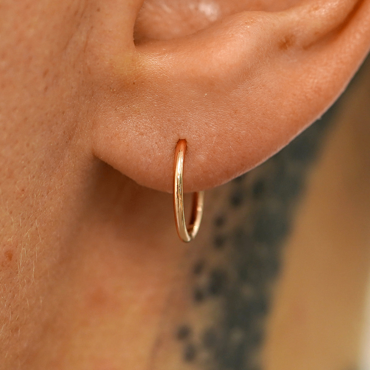A model's ear wearing a 14k rose gold Medium Seamless Huggie Hoop / Piercing