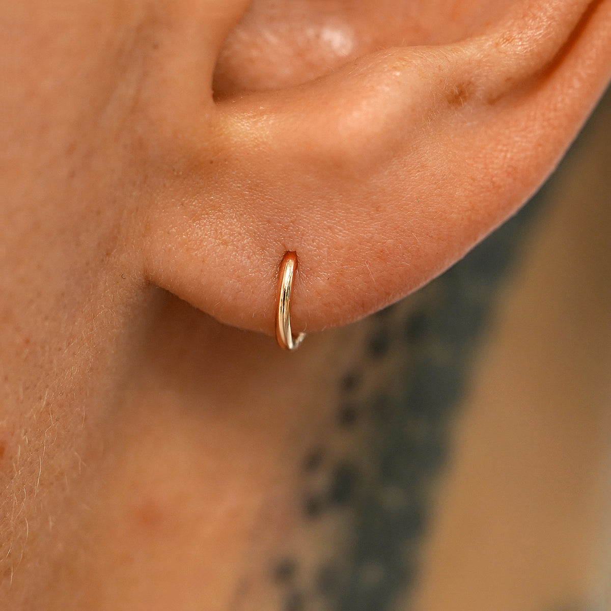 A model's ear wearing a 14k rose gold Mini Seamless Huggie Hoop / Piercing