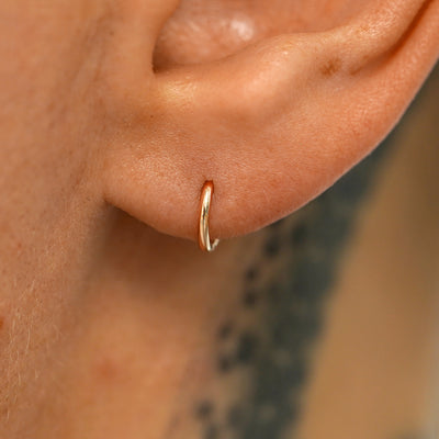 A model's ear wearing a 14k rose gold Mini Seamless Huggie Hoop / Piercing
