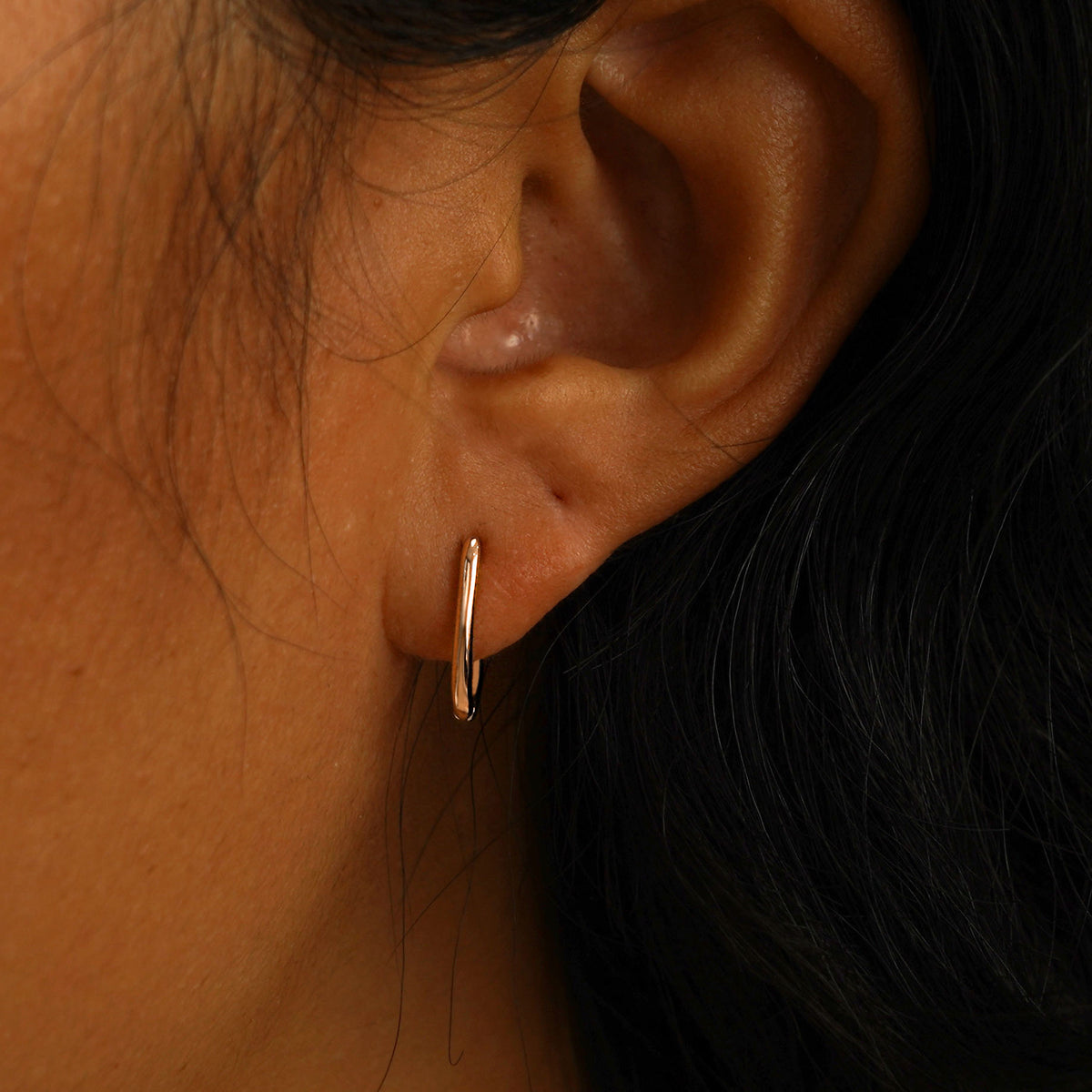 A model's ear wearing a 14 karat rose gold Oval Huggie Hoop