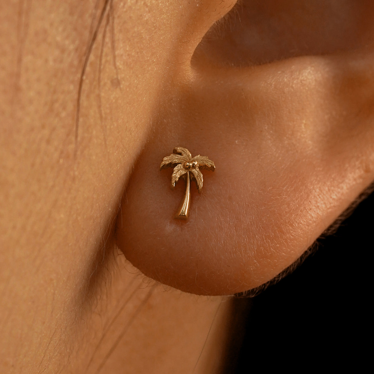 Close up view of a model's ear wearing a 14k rose gold Palm Tree Earring