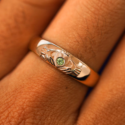 Close up view of a model's fingers wearing a 14k rose gold peridot Gemstone Claddagh Band