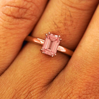 Close up view of a model's fingers wearing a 14k rose gold Emerald Cut Lab Pink Sapphire Ring