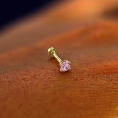 A solid 14k rose gold pink sapphire Piercing resting on the back of a model's hand