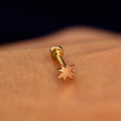 A rose gold 8 pointed star flatback piercing with yellow gold backing on a models hand