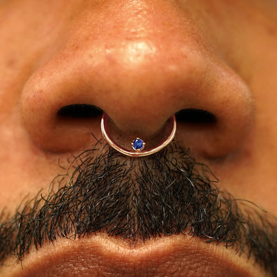 Close up view of a model's nose wearing a 14k rose gold sapphire Raised Gemstone Septum