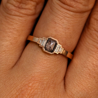 Close up view of a model's hand wearing a 14k rose gold Emerald Cut Salt and Pepper and Clear Baguette Diamond Ring