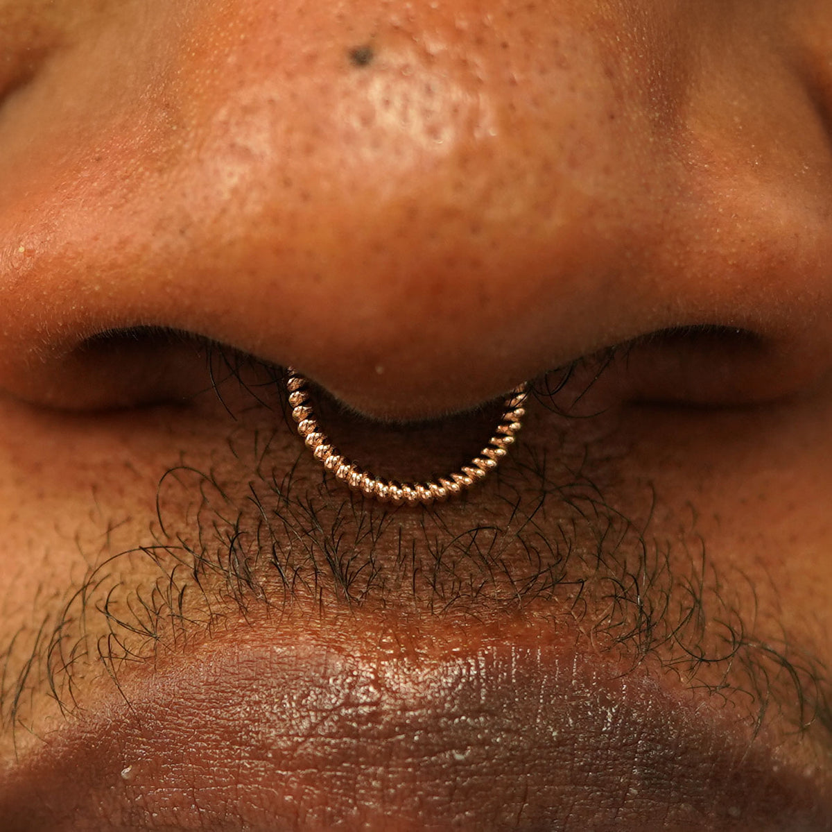 Close up view of a model's nose wearing a 14k rose gold Rope Septum