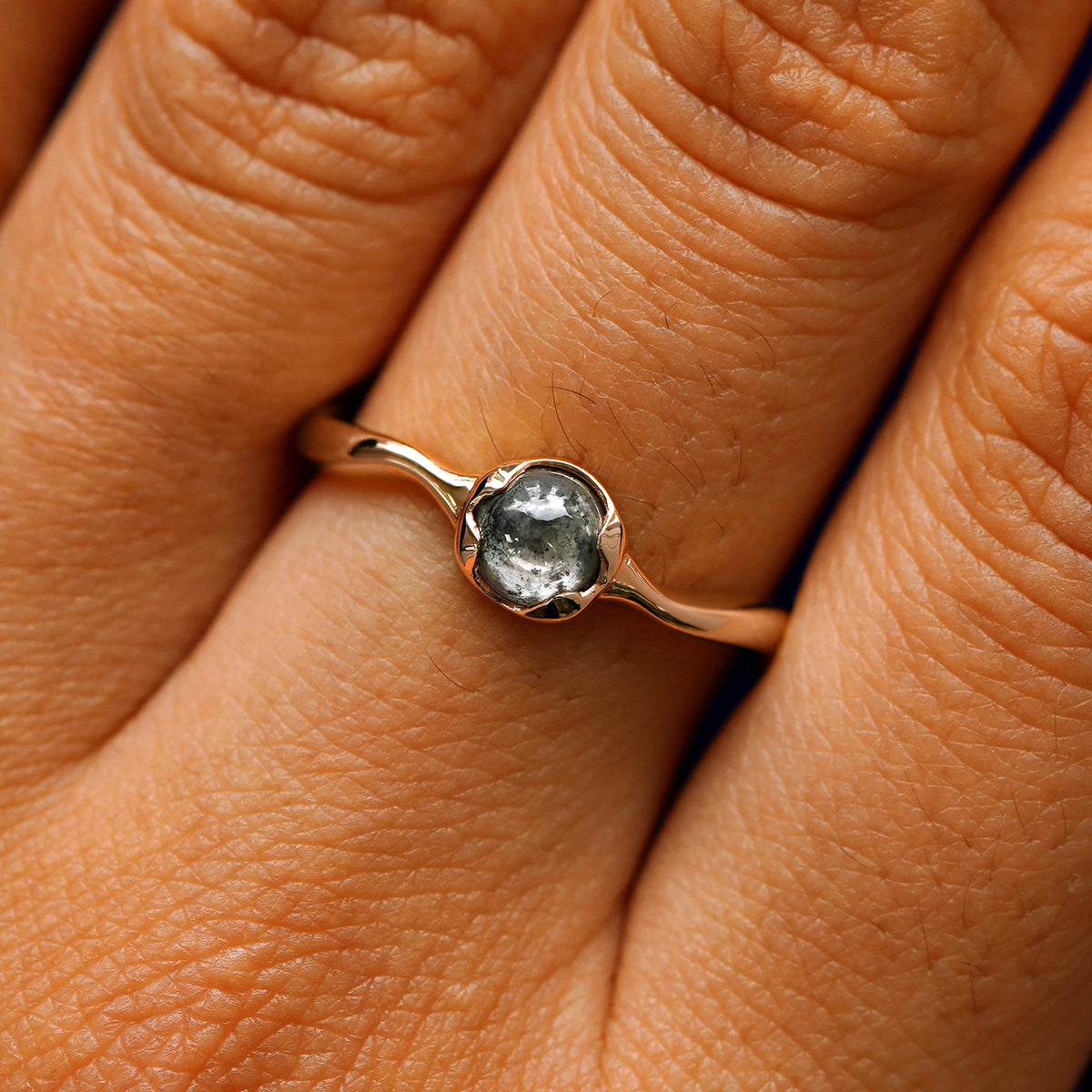 Close up view of a model's hand wearing a 14k rose gold round cabochon salt and pepper diamond ring