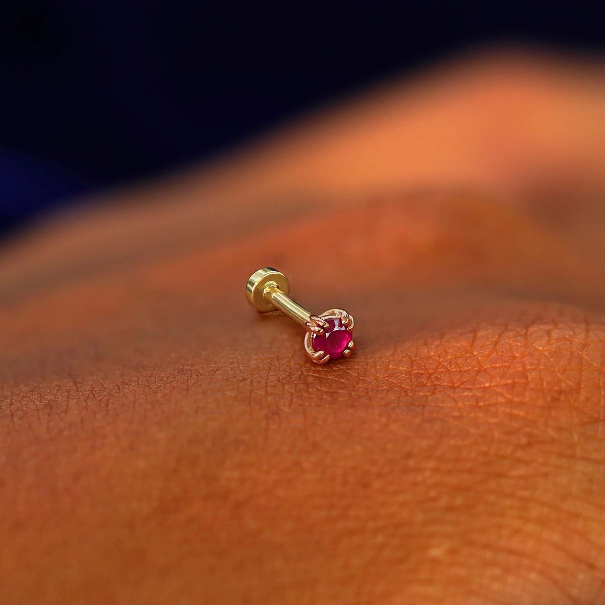 A solid 14k rose gold Ruby Flatback Piercing resting on the back of a model's hand
