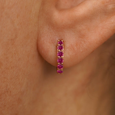 Close up view of a model's ear wearing a rose gold Small Ruby Huggie Hoop