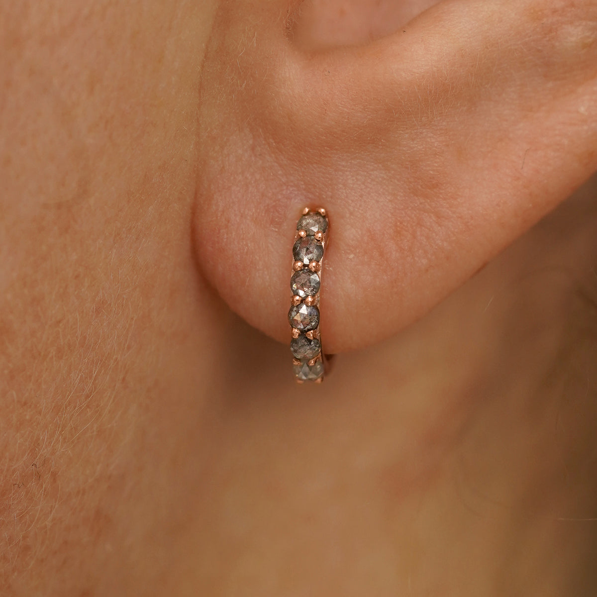 Close up view of a model's ear wearing a rose gold Small Salt and Pepper Diamond Huggie Hoop