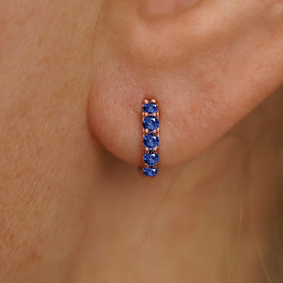 Close up view of a model's ear wearing a rose gold Mini Blue Sapphire Huggie Hoop