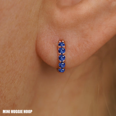 Close up view of a model's ear wearing a rose gold Mini Blue Sapphire Huggie Hoop