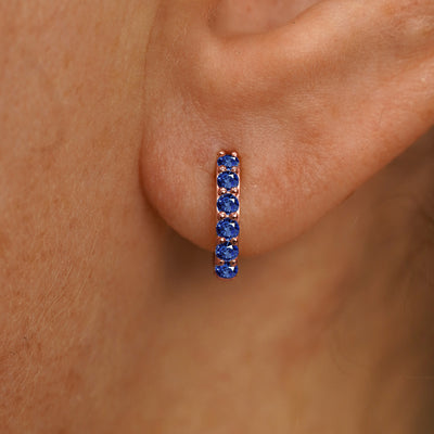 Close up view of a model's ear wearing a rose gold Small Blue Sapphire Huggie Hoop