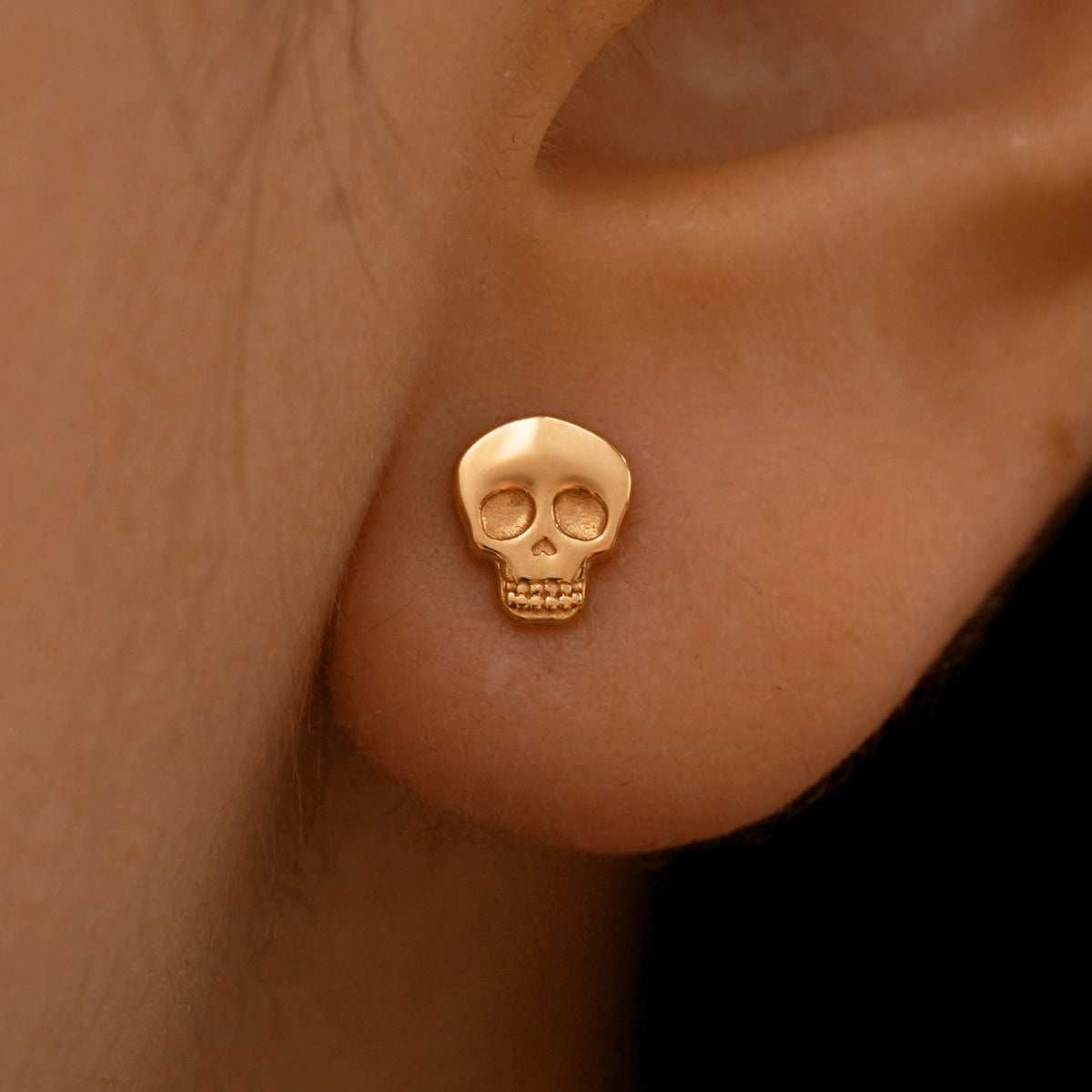 Close up view of a model's ear wearing a 14k rose gold Skull Earring