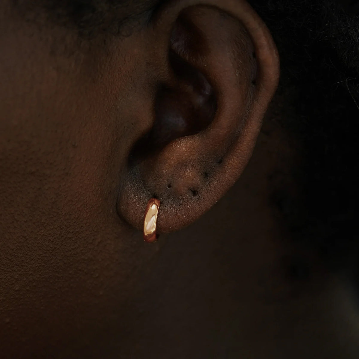 Close up view of a model's ear wearing a 14k rose gold Small Wide Huggie Hoop Earring