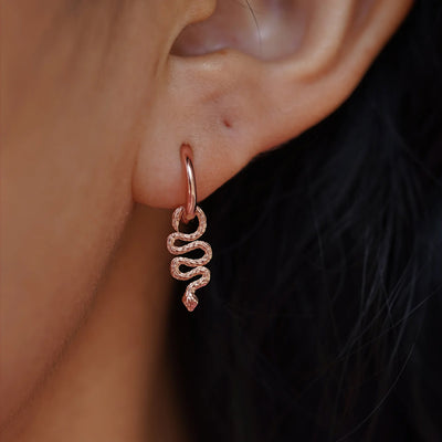 Close up view of a model's ear wearing a rose gold Snake Charm on a Curvy Huggie Hoop