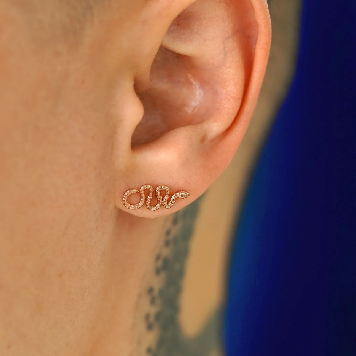 A model's ear wearing a 14k rose gold Snake Earring with the snake horizontal