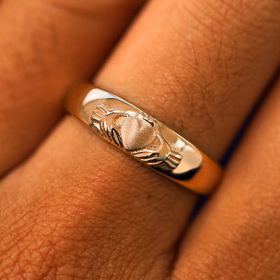 Close up view of a model's fingers wearing a 14k rose gold Claddagh Band