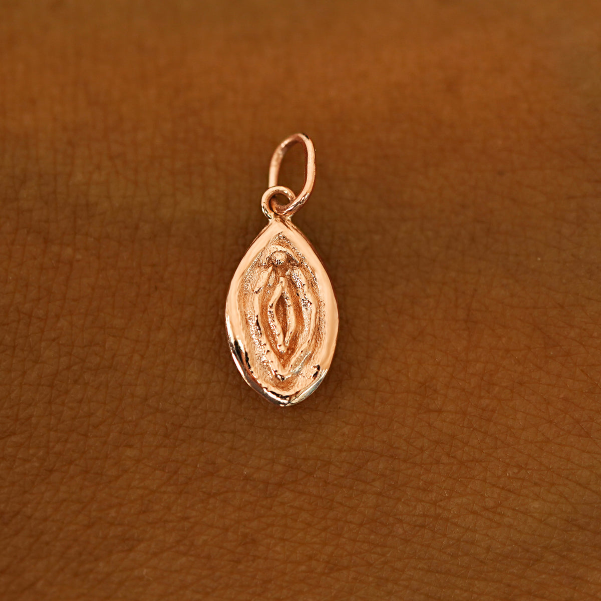 A solid 14k rose gold Vulva Charm resting on the back of a model's hand
