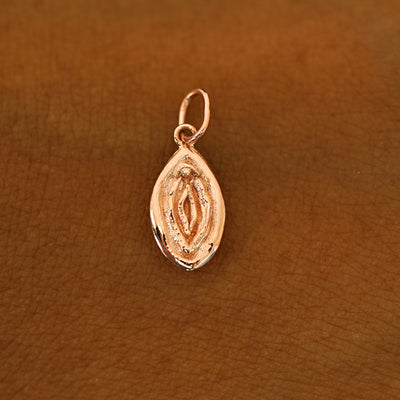 A solid 14k rose gold Vulva Charm resting on the back of a model's hand