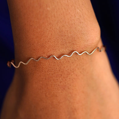 Close up view of a model's wrist wearing a 14k  rose gold Wave Bangle Bracelet