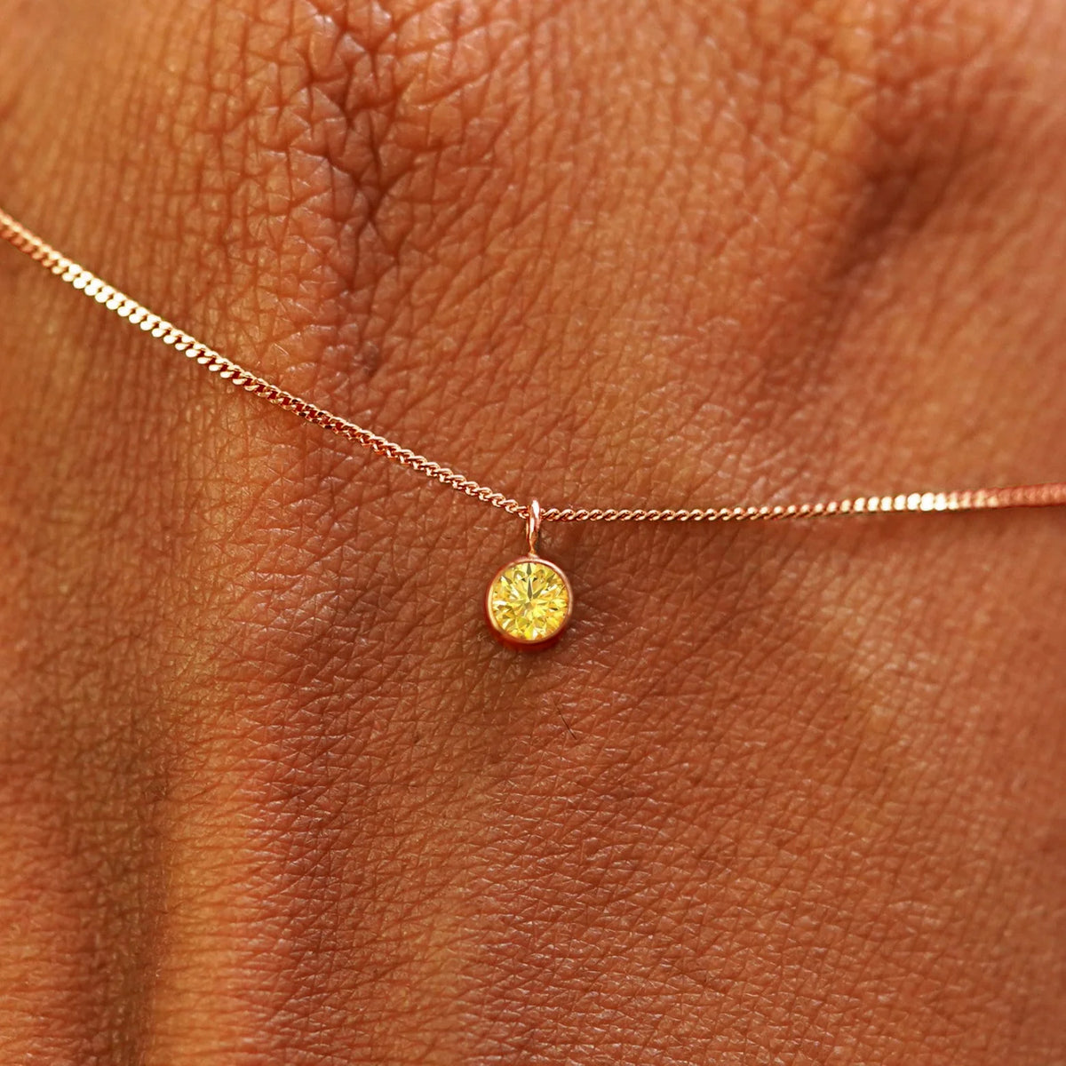 Close up view of a 14k rose gold Yellow Diamond Necklace draped across the back of a model's hand