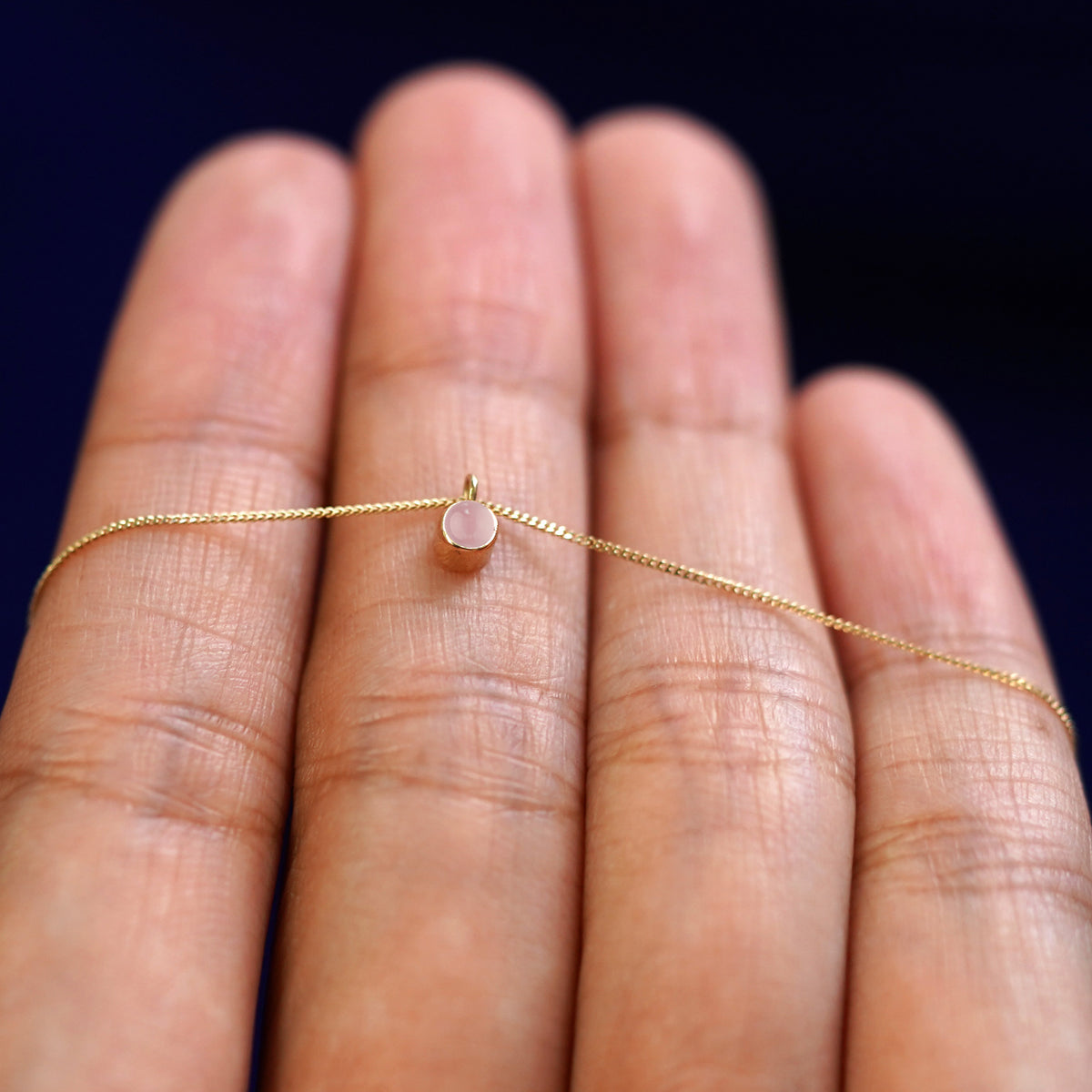 A 14k gold Rose Quartz Necklace draped over a model's fingers